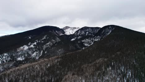 Panning-drone-shot-of-a-snow-covered-mountain-peak-with-fast-moving-clouds