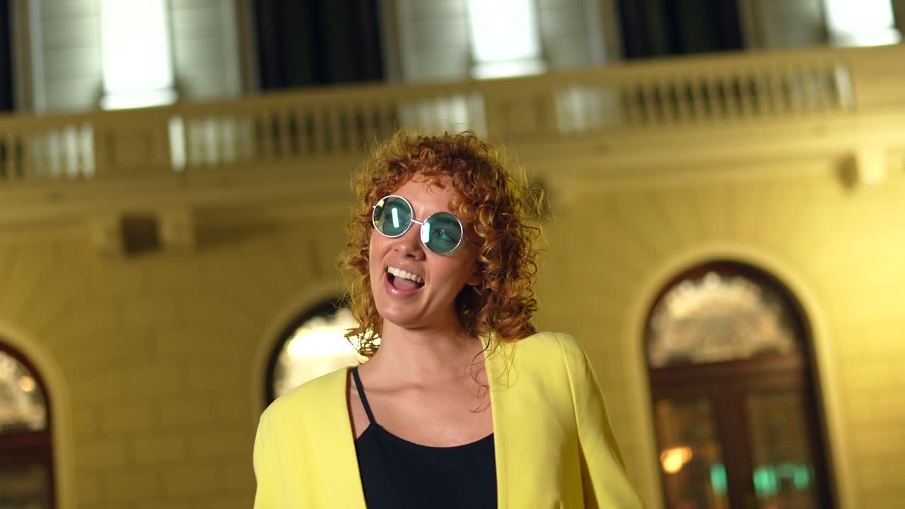 Woman in yellow blazer wearing sunglasses at night