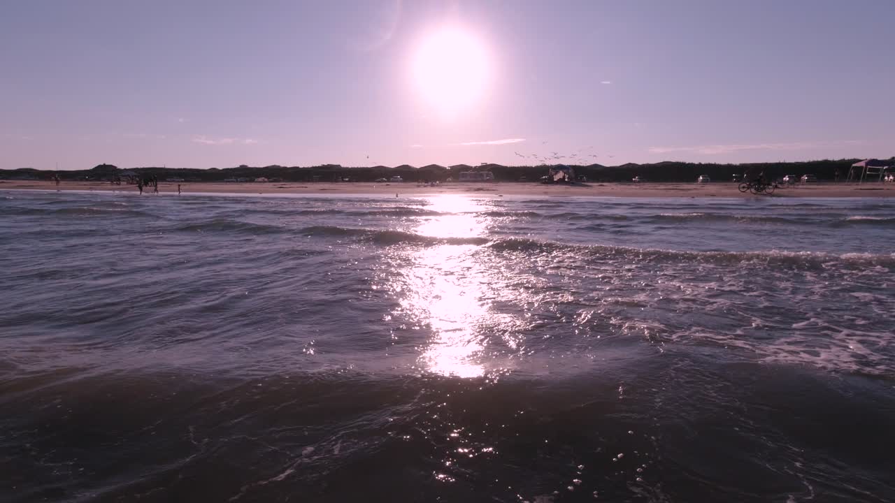 The waves from the Gulf of Mexico break onto the beach in Port Aransas, Texas while people watch the sunset.