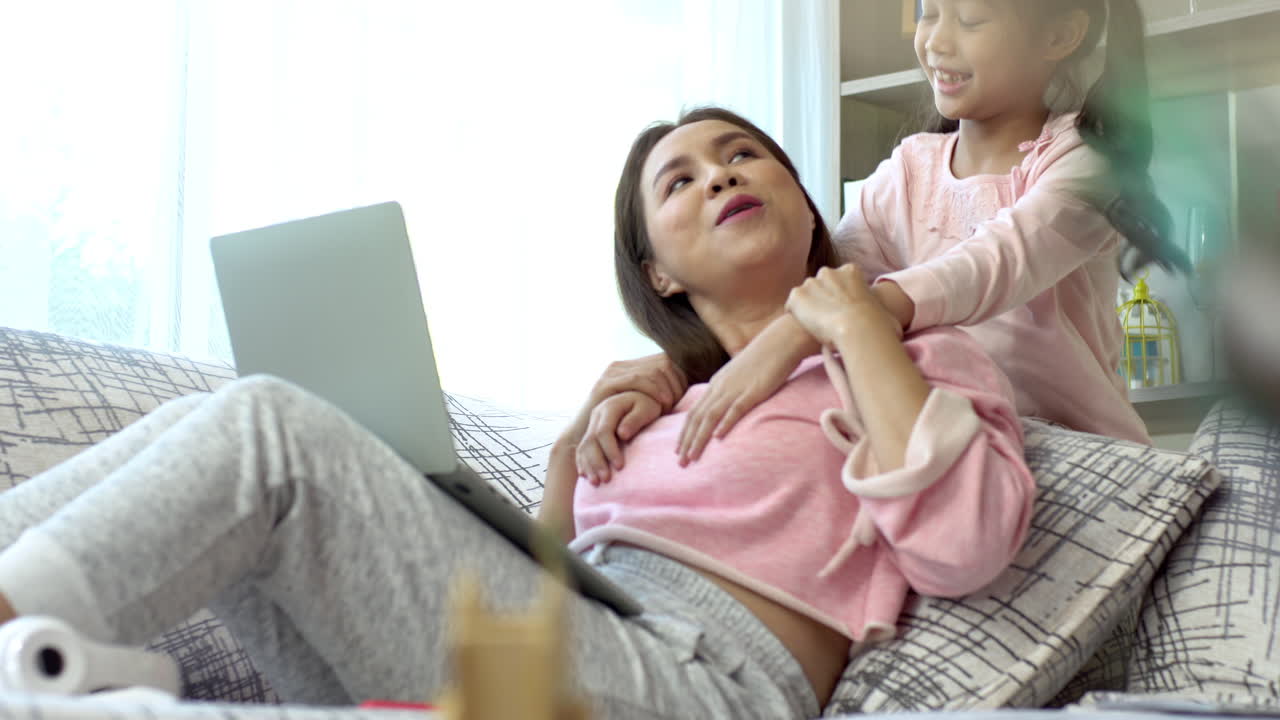 A Beautiful Asian mother busy working at home while looking after and teaching her children on a laptop computer