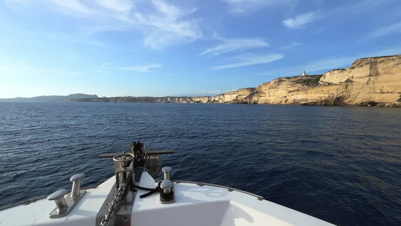 Punto de vista de la proa de un velero navegando hacia los acantilados de la isla de Córcega y el faro de Capo Pertusato en Francia, a cámara lenta