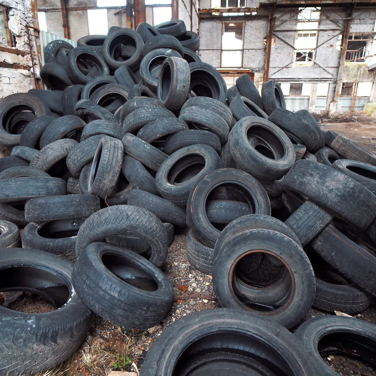 Old broken-down building inside with many tires on a large bunch. Black used rubber tires of vehicles on a desolate plant