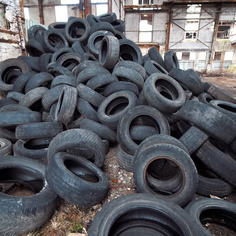 old broken-down building inside with many tires on a large bunch. black used rubber tires of vehicles on a desolate plant