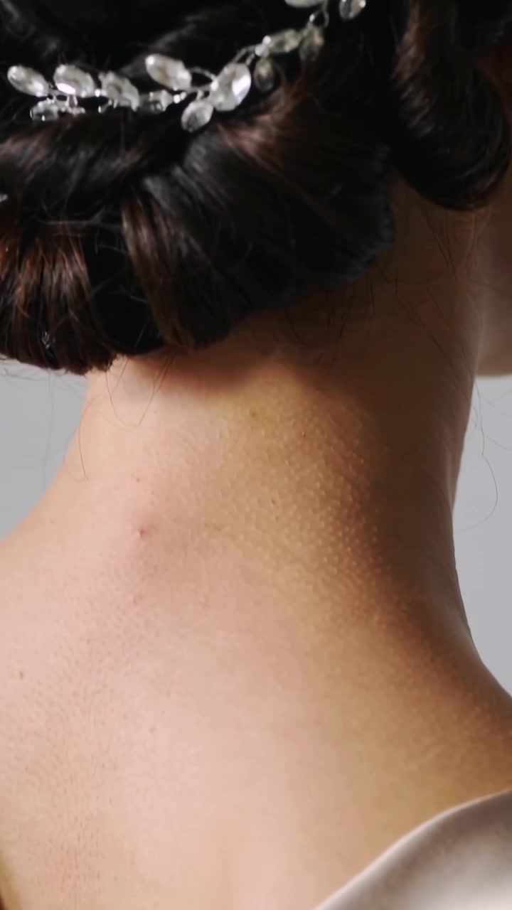 Video verticale: Rivelazione dello chignon di una donna mentre la telecamera scorre verso il basso in un set, mostrando una clip di cristallo e una spallina del vestito.