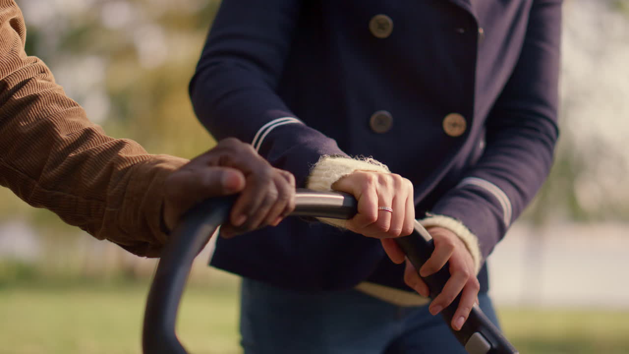 los padres con las manos en el cochecito empujando el carruaje de bebé de cerca. una pareja casada feliz.