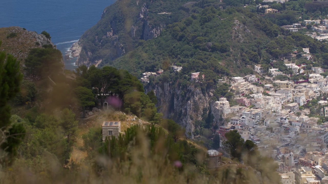 Inquadratura ravvicinata statica che cattura gli iconici edifici bianchi di Capri con la natura montuosa circostante sullo sfondo.