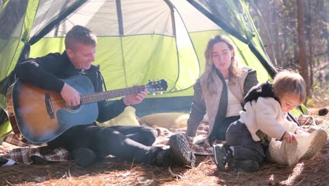 a man plays guitar by a cozy tent joyfully entertaining family a man plays guitar in front of a cozy tent surrounded by family and two children creating joyful memories and highlighting togetherness