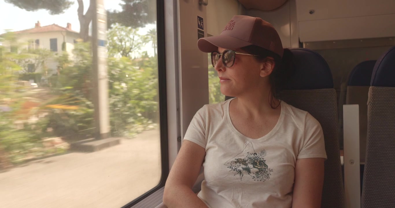Donna con occhiali da sole guarda fuori dal finestrino del treno il paesaggio illuminato dal sole nel sud della Francia