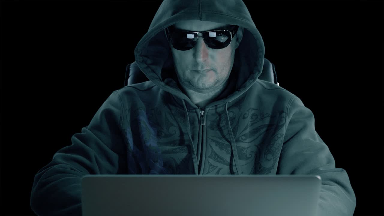 un hombre con capucha y gafas sentado en la mesa y codificando en el portátil. noche oscura. hacker con gafas trabajando en la computadora. codificando hombre en fondo de hormigón. canal alfa clave de croma fondo transparente.