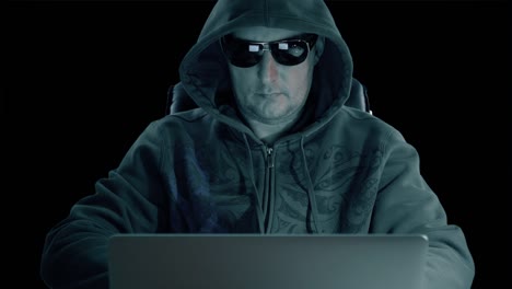 un hombre con capucha y gafas sentado en la mesa y codificando en el portátil. noche oscura. hacker con gafas trabajando en la computadora. codificando hombre en fondo de hormigón. canal alfa clave de croma fondo transparente.