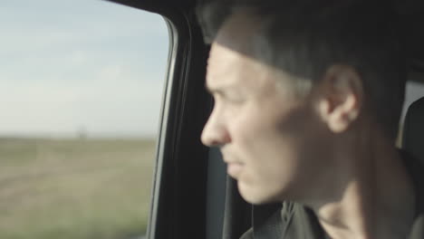 soft focus on closeup of a man's face as he stares out the window of a car with a rack focus to his face as he looks forward