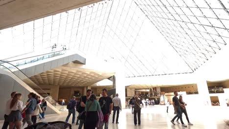 personas caminando dentro de la entrada de la pirámide de vidrio del museo del louvre