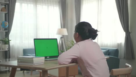 teenage girl sitting at her desk learning online on a laptop with green mock-up