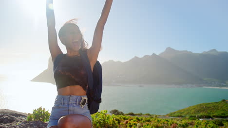 portrait of woman with backpack on vacation taking a break on hike by sea stretching arms in the air