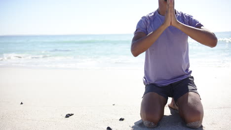 Un-Joven-Birracial-Está-Meditando-En-La-Playa,-Con-Las-Manos-Juntas-En-Una-Pose-De-Oración,-Con-Copia-