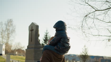 a close-up of a father carrying his son on his shoulders playfully, the father wears a brown jacket, and the son wears a black jacket, with a blurred cityscape view