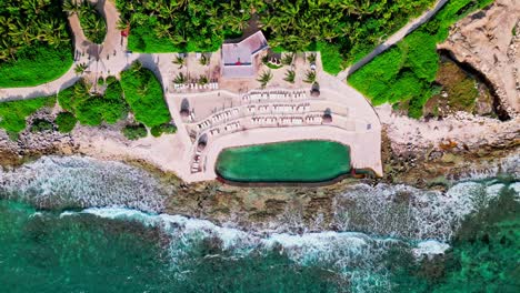 Trs-Yucatan-Resort-En-Tulum-México-Vista-Estática-Hacia-Abajo-De-La-Piscina-De-Agua-Salada-Con-Olas-Rompiendo-En-La-Orilla-Rocosa