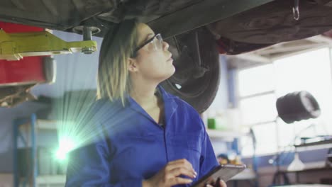 Animation-of-glowing-light-over-biracial-woman-working-in-car-workshop