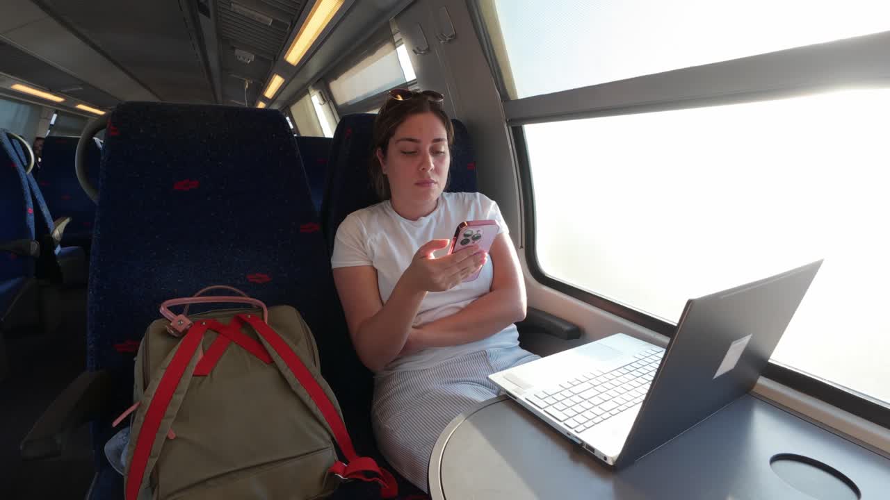 Woman Using Smartphone and Laptop on a Public Train