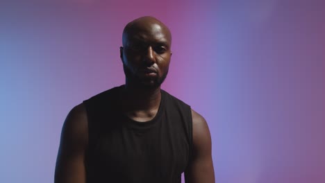 studio portrait shot of male athlete wearing sports vest against pink and blue lit background