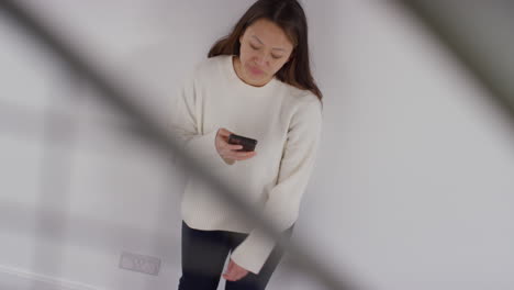 스트레스를 받거나 불안한 여성이 집에서 벽에 기대어 인터넷이나 소셜 미디어 뉴스 메시지 또는 휴대 전화에 반응하는 오버헤드