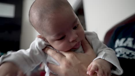 padre sosteniendo suavemente a su hijo de 2 meses en su frente para ayudarlo a eructar después de beber leche en su regazo