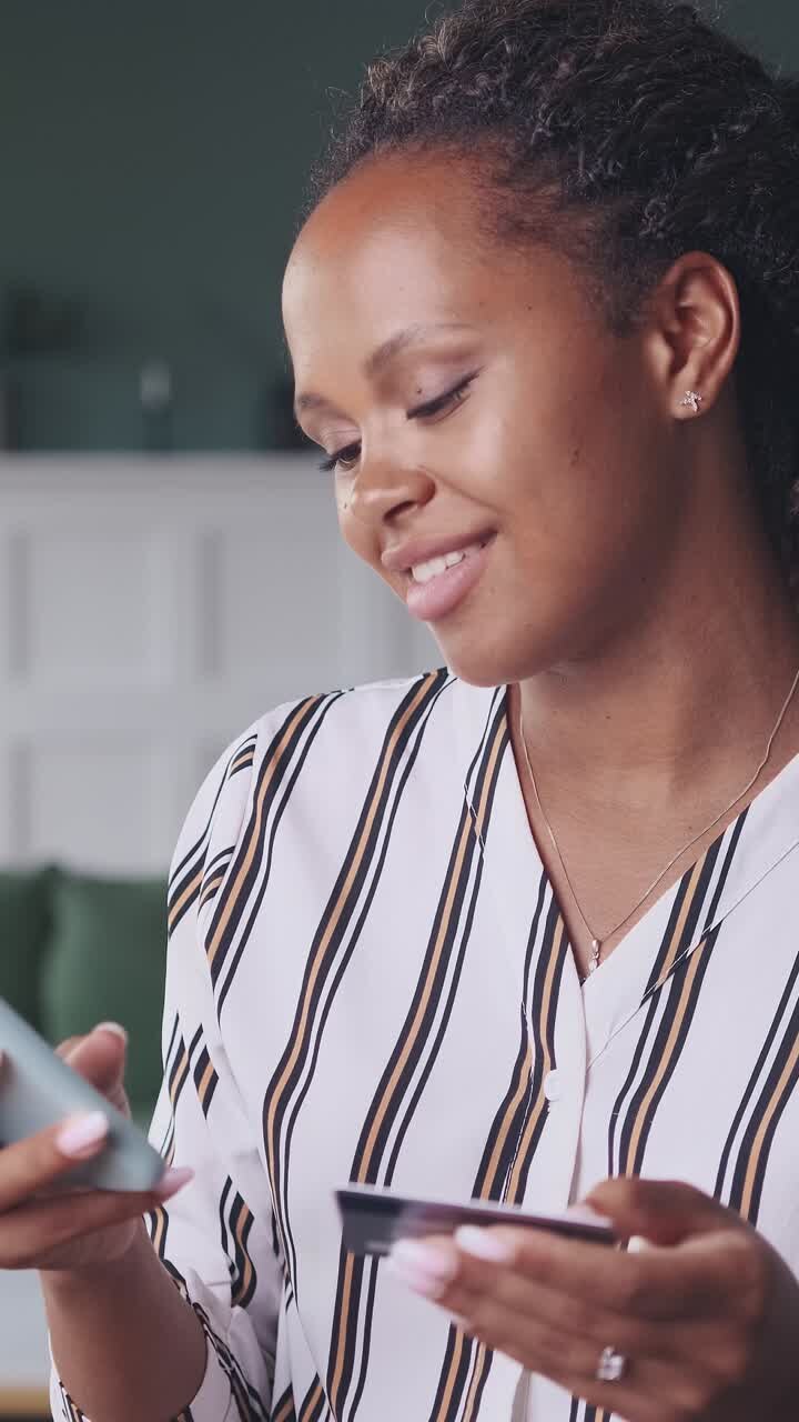 Young successful african american woman shopaholic uses credit card and phone