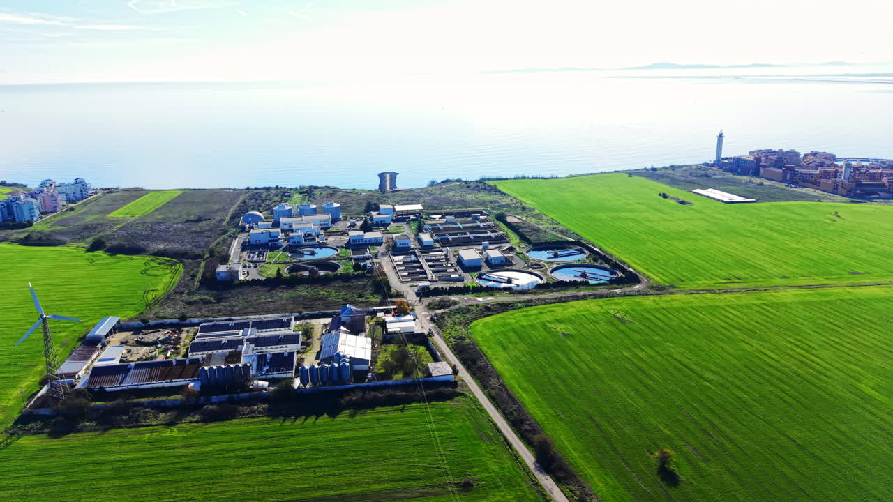 High angle aerial view showing a water treatment plant, agricultural fields, and a coastal town with a lighthouse in the background