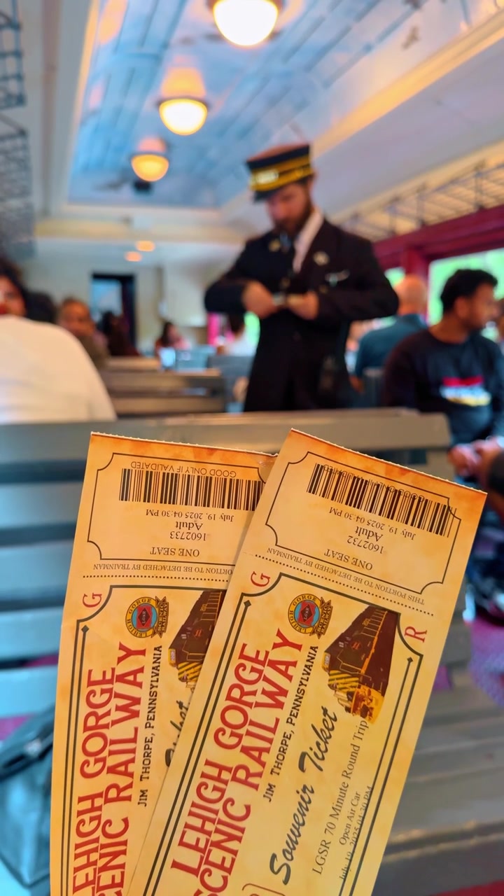 Jim Thorpe, USA, 2 July 2025: Close up of hands holding two yellow souvenir tickets. Two paper souvenir railway tickets held in focus with a blurred conductor in uniform standing in the background.