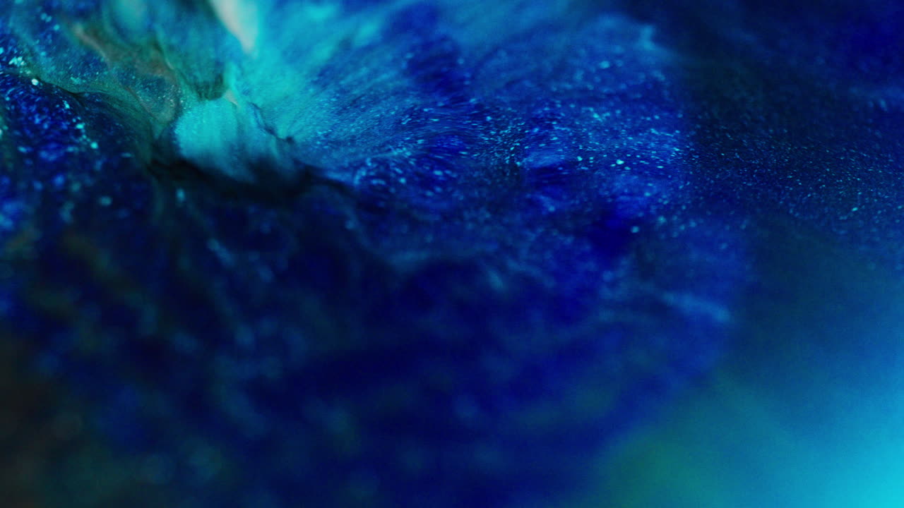 Macro shot of blue and white glittery inks reacting under pressure, forming abstract, inflated patterns in motion