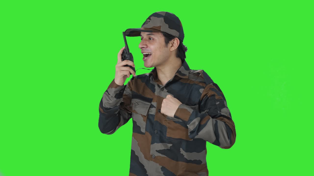 Uomo dell'esercito indiano felice che dà istruzioni con un walkie-talkie, schermo verde