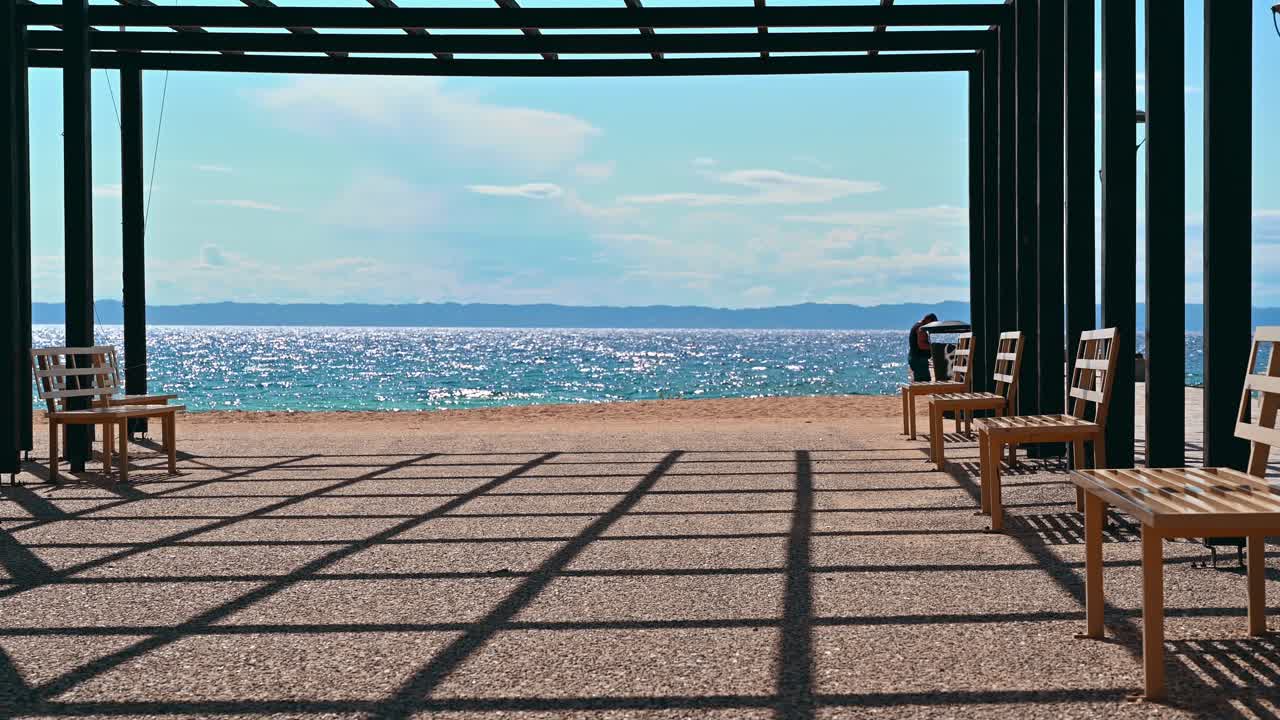 A gazebo on a pier with black metal posts and a benches, Aegean sea in Nikiti, Greece. Slow motion, zooming out effect