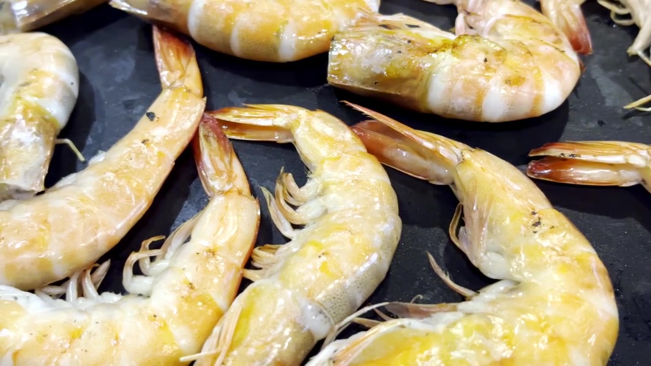 Primo piano di gamberi freschi che sfrigolano su una padella calda da barbecue, catturando frutti di mare succosi, vapore che sale e deliziosi sapori grigliati in una scena di cucina.