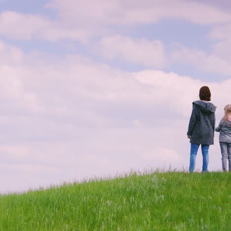 A-Family-Of-Three-People---Father-Mother-And-Daughter-6-Years-Old-Stand-On-Top-Of-A-Green-Hill