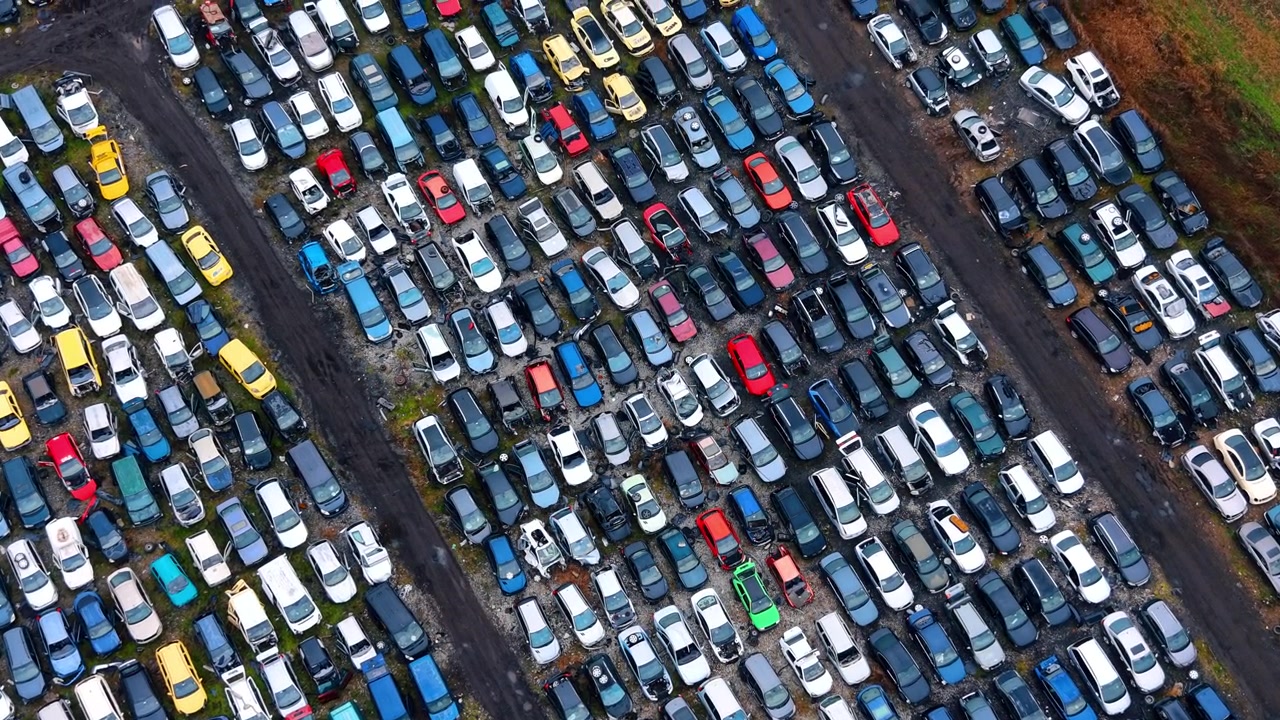 Perspektivbillede fra høj vinkel af rækker på en bilkirkegård. Diagonalt overblik ovenfra af forskellige gamle og beskadigede biler parkeret tæt i parallelle rækker.