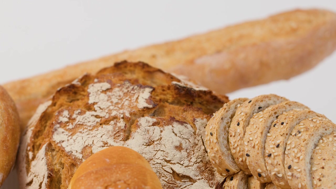 Una mano afferra un mucchio di pane a lievitazione naturale, baguette e pagnotte multicereali su sfondo bianco.