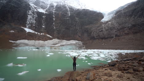 vista trasera, mujer joven levantando los brazos frente al pintoresco lago glacial y al glaciar