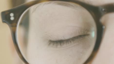Detail-of-a-girl's-eye-opening,-she-is-wearing-glasses-and-the-eye-is-seen-through-the-lens-and-frame,-slow-motion
