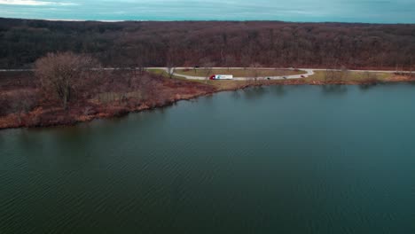 cinematic aerial of a red semi truck and white trailer parked on side of a lake