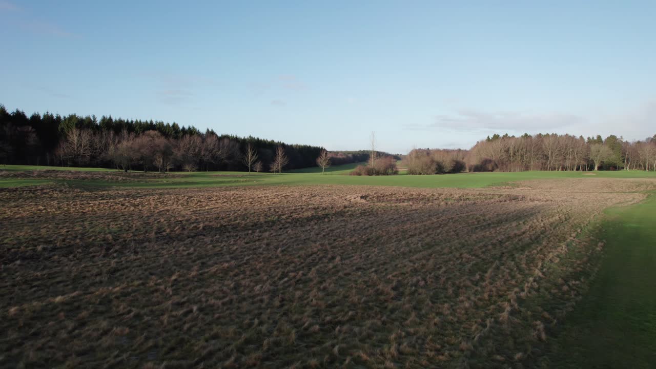 Low Lever Drone Flying, Field and Golf Course Surrounded by Forest - Dolly In Shot