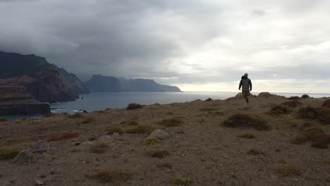 aerial is following a young man that is running towards the edge of the cliff at sao laurenco, madeira