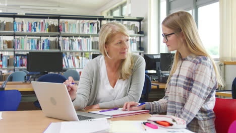 teacher and female student work on computer in college library