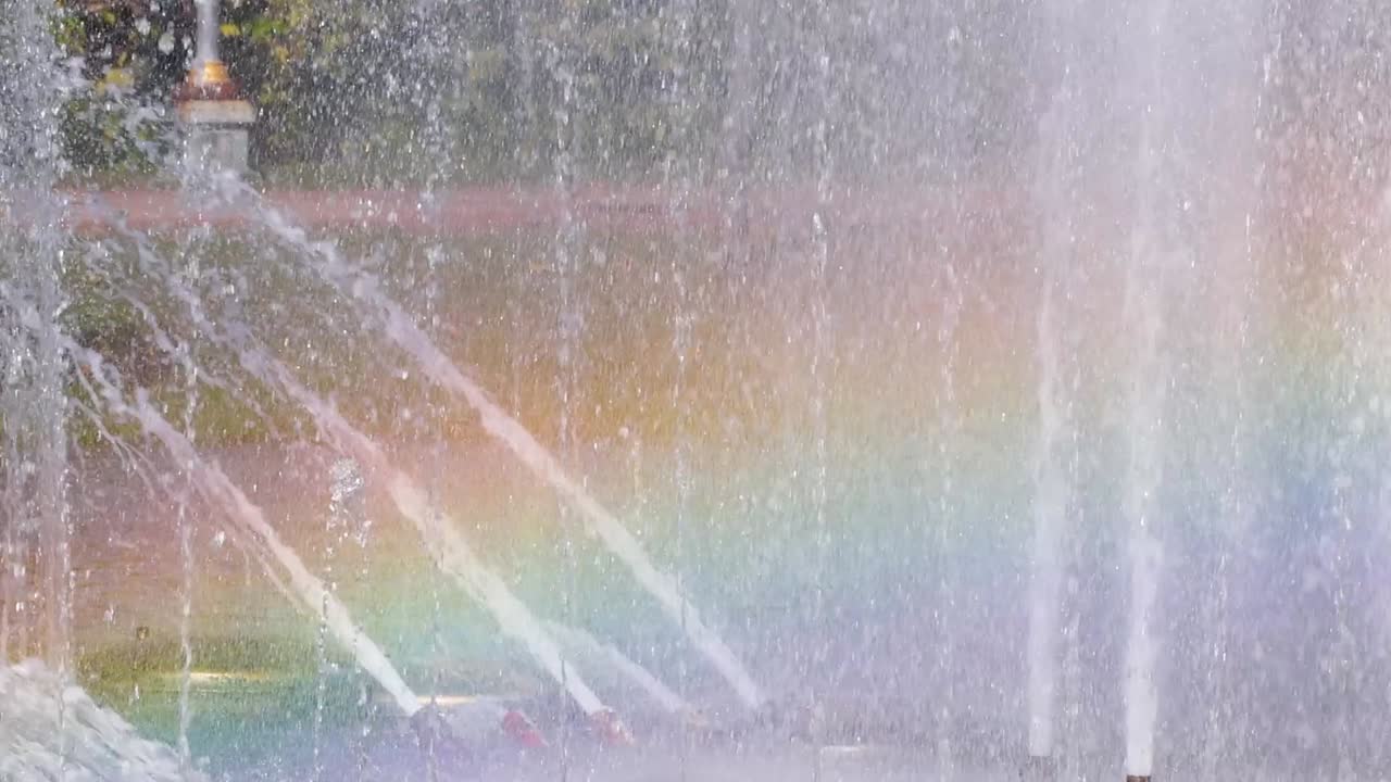 A vivid rainbow forms amidst the cascading water jets of a fountain, showcasing a beautiful spectrum of colors.