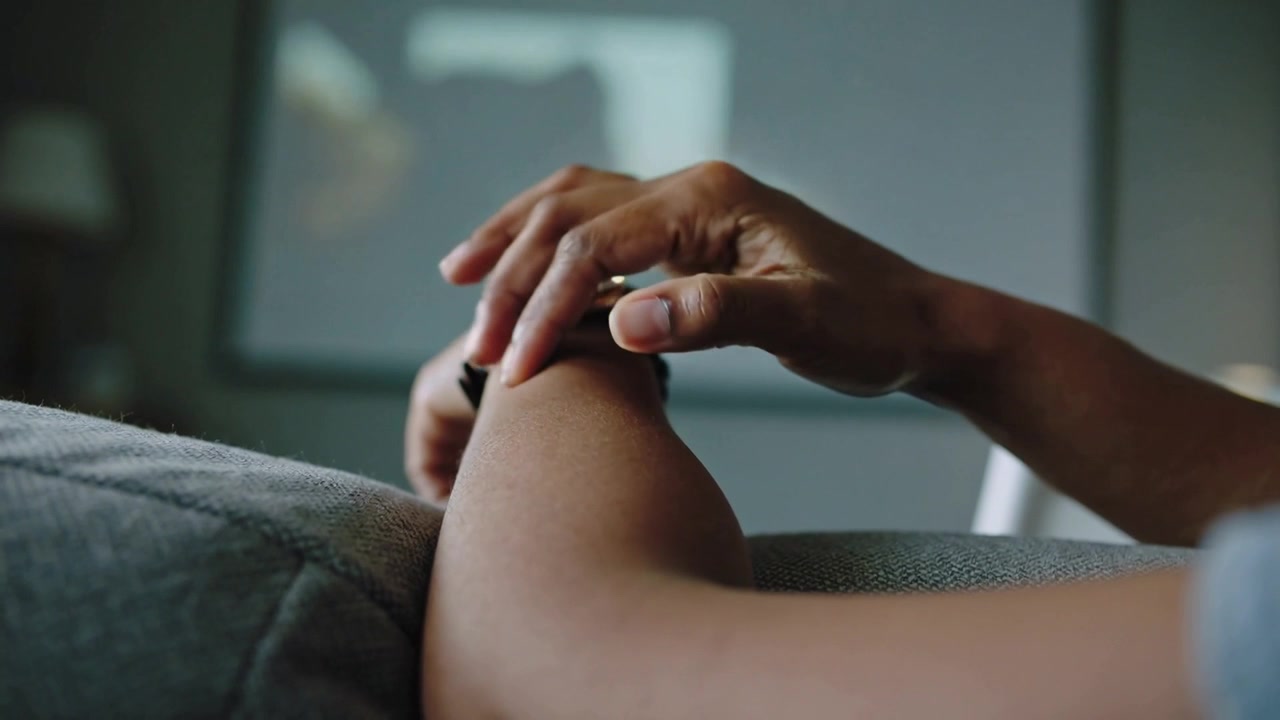 Pressing and rubbing hand reaching forearm on armrest at home wearing grey shirt with watch