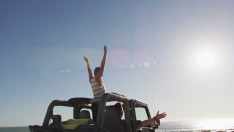 happy caucasian gay male couple in car raising arms and waving on sunny day at the beach