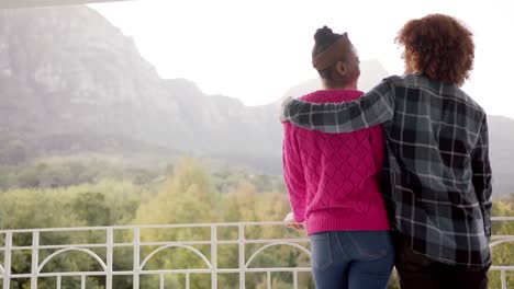 Rear-view-of-happy-diverse-couple-embracing-and-talking-on-balcony-overlooking-garden,-slow-motion