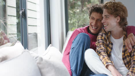 Happy-diverse-gay-male-couple-looking-through-window-and-embracing-at-home,-slow-motion,-copy-space