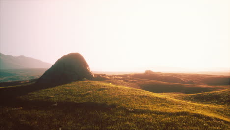 sunrise over a grassy hill with a rock