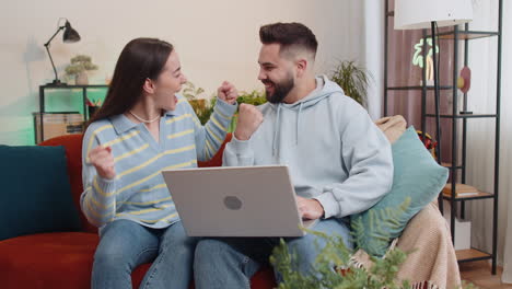 family couple man woman working on laptop celebrate success win money in lottery online good news