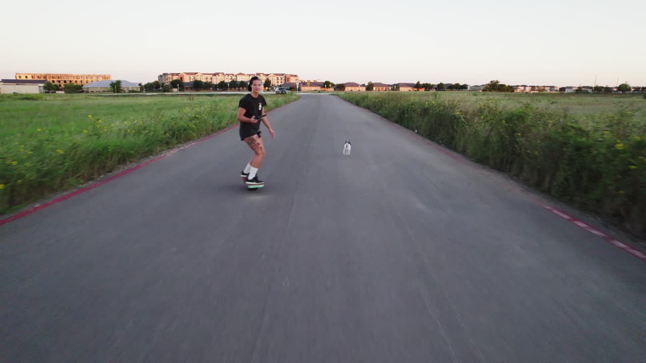 Aerial shot of someone cruising on a Onewheel through a grassy field, dog by their side